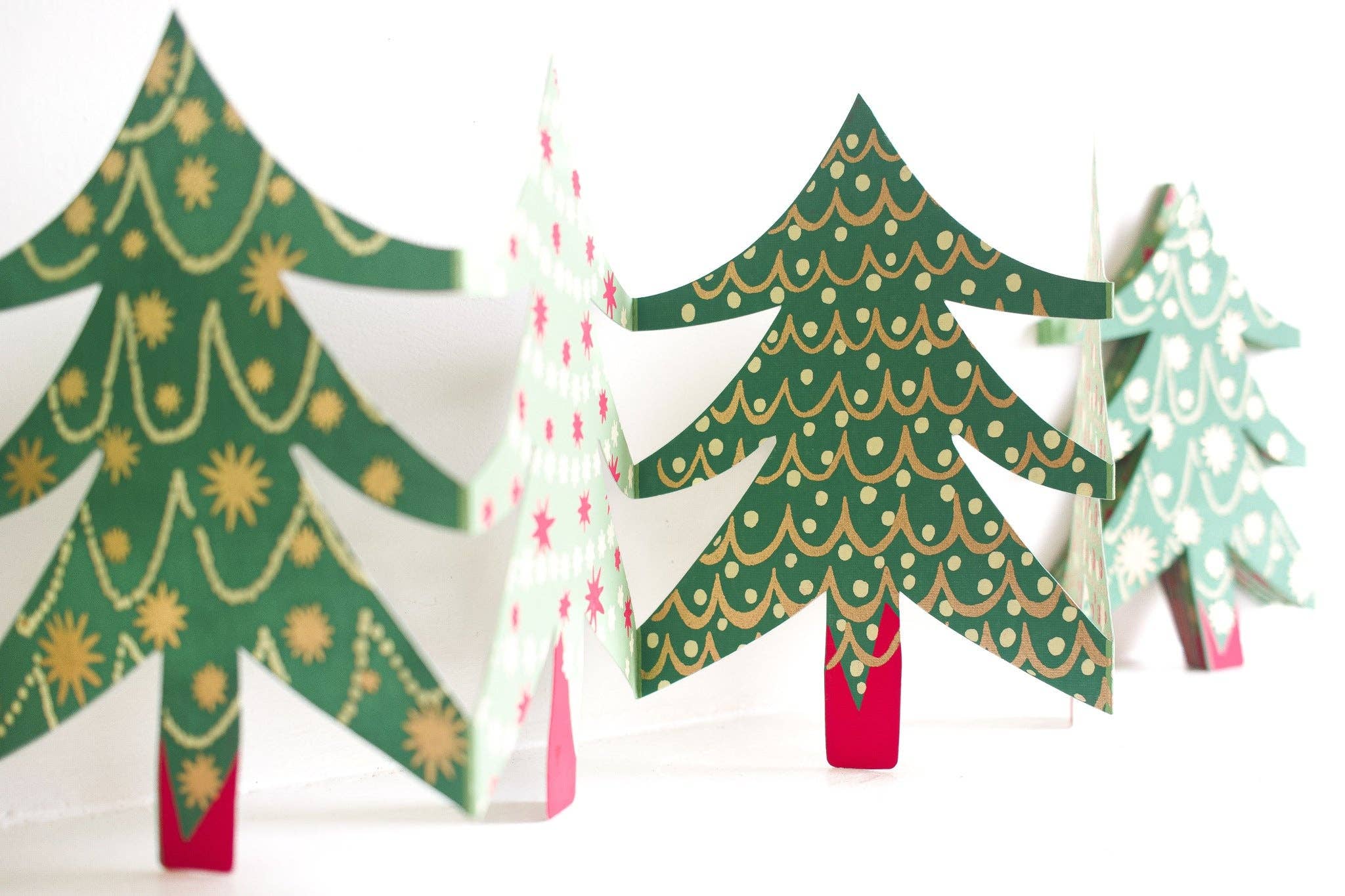 Decorative paper Christmas trees with green, red, and white patterns on a white background.