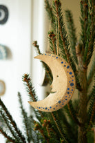 Wooden moon-shaped ornament with star patterns hanging on a Christmas tree.