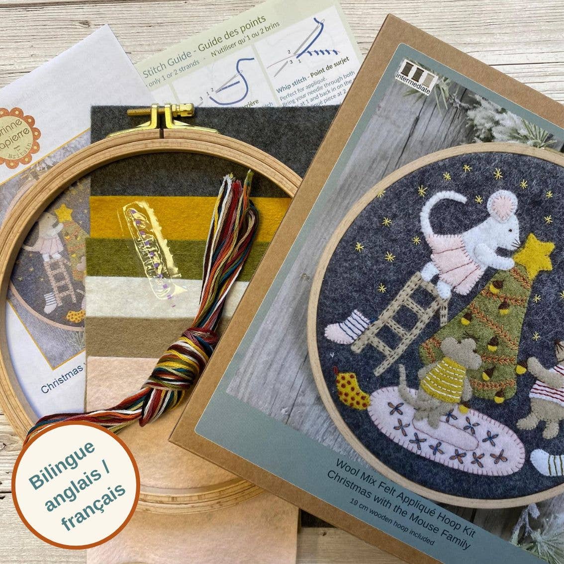 Embroidery hoop kit with Christmas-themed design, including a mouse family on a ladder, on a wooden surface.