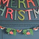 Decorative Christmas letter banner on a dark surface with green and red colors.