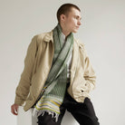 Man wearing a beige jacket and green scarf against a plain background