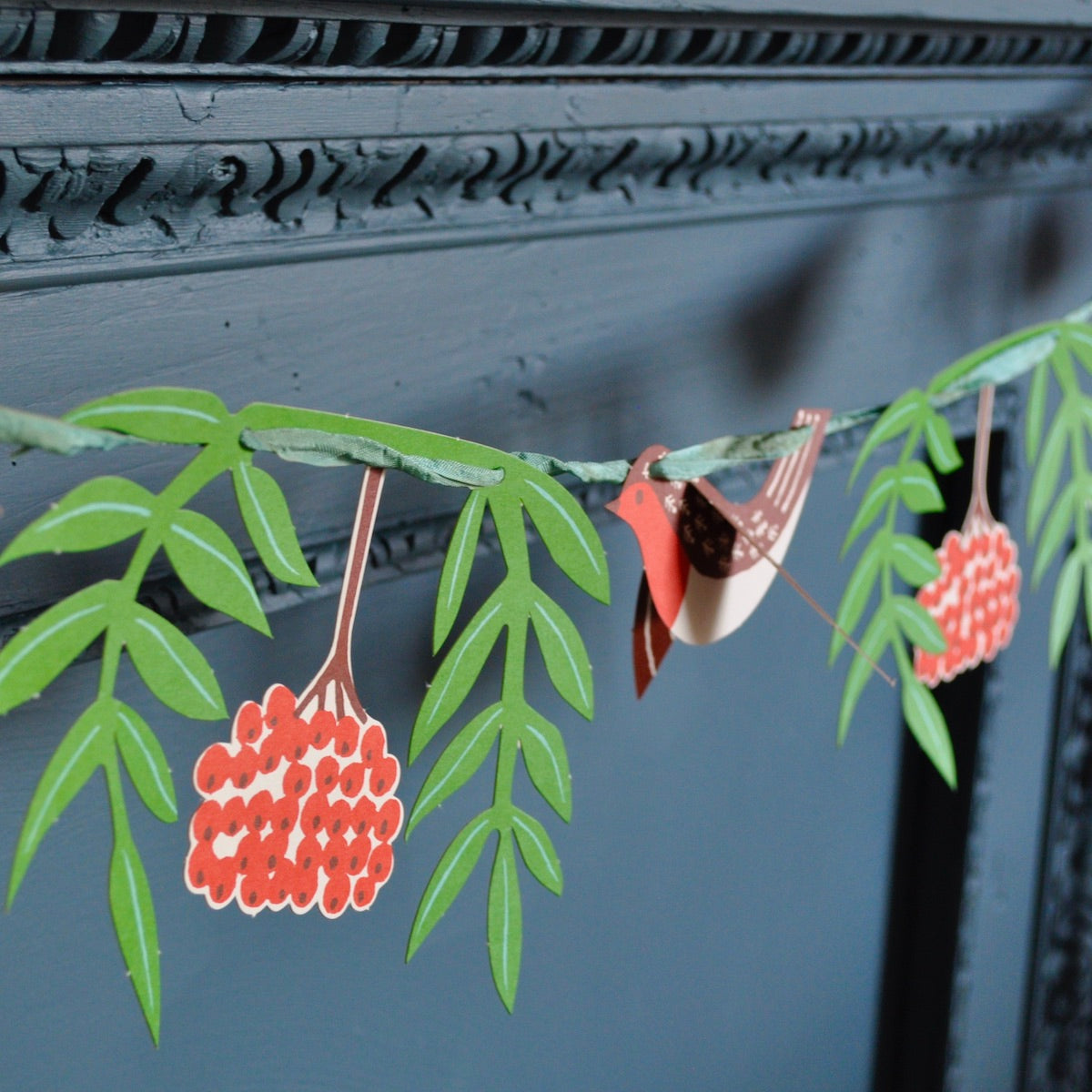 Decorative garland with green leaves and red berries hanging against a dark background