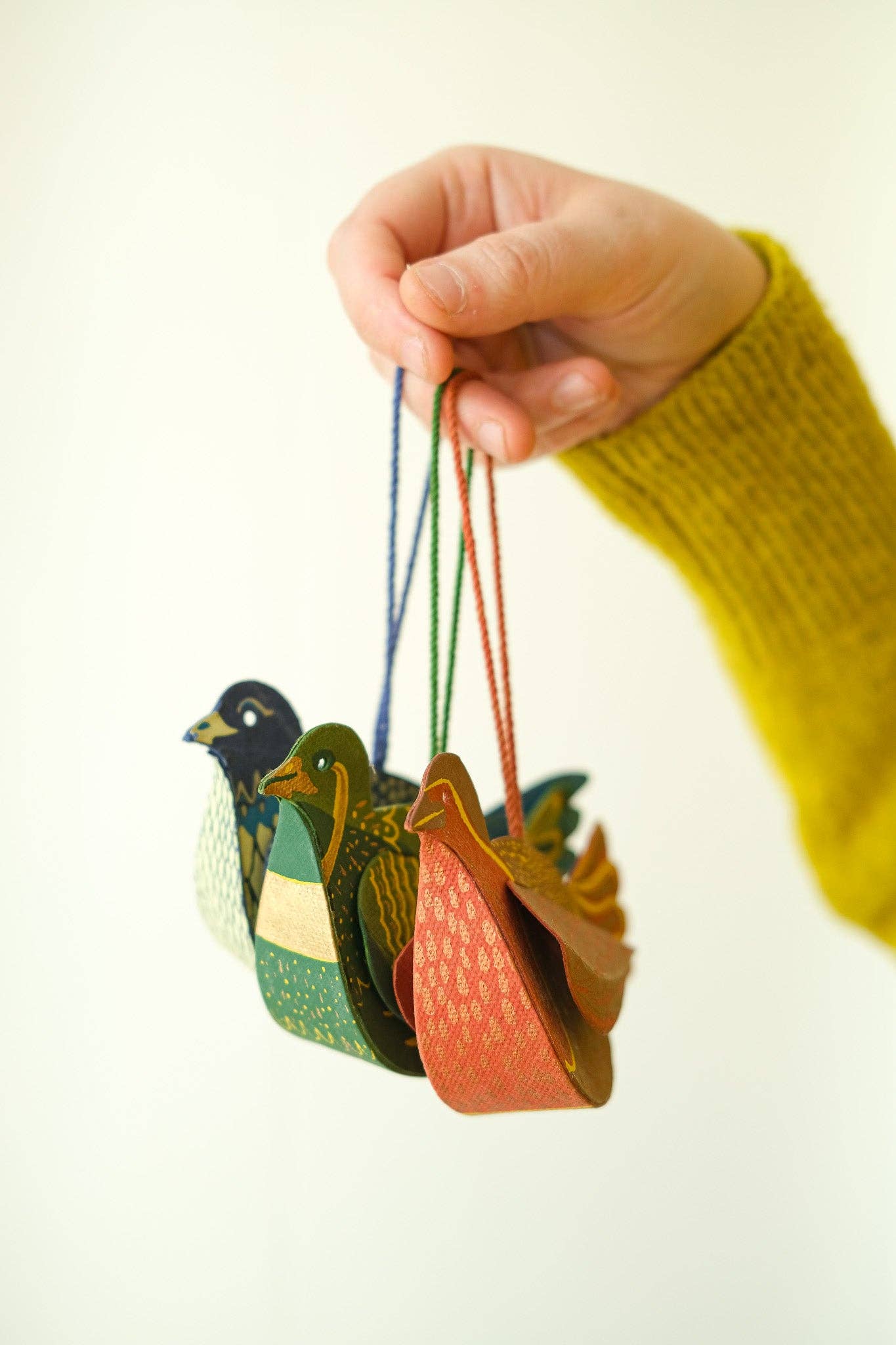 Colorful duck-shaped tea infusers hanging from a string held by a hand.