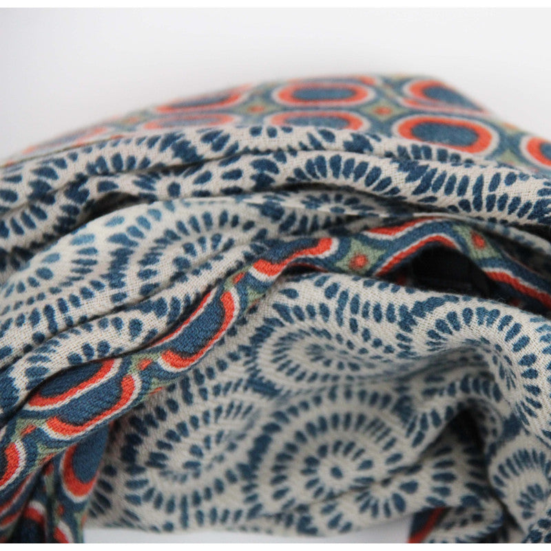 A close-up of a folded patterned fabric with a blue and red circular and spiral motif on a light background.