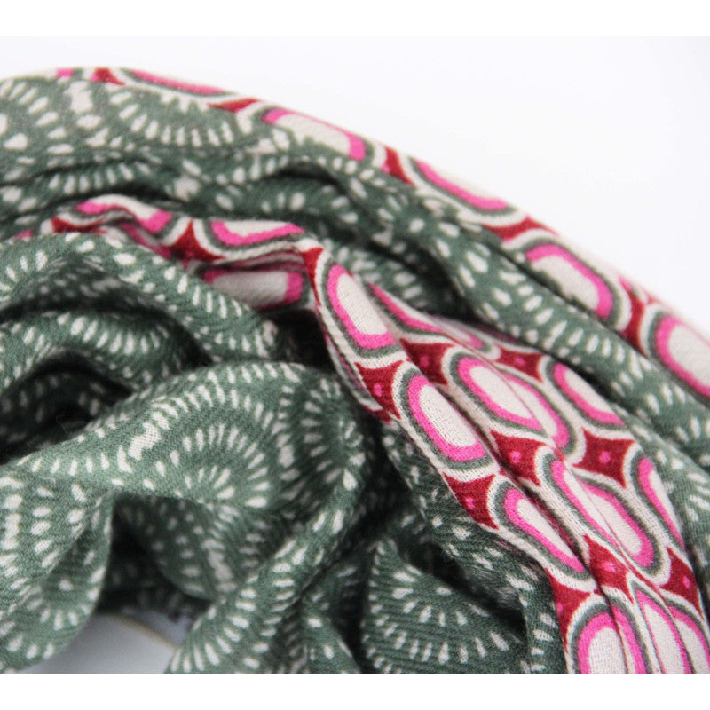 A close-up of a patterned fabric or scarf with two distinct designs: one side features a sage green and white geometric wave pattern, while the other side displays a red, pink, and white paisley-like pattern.