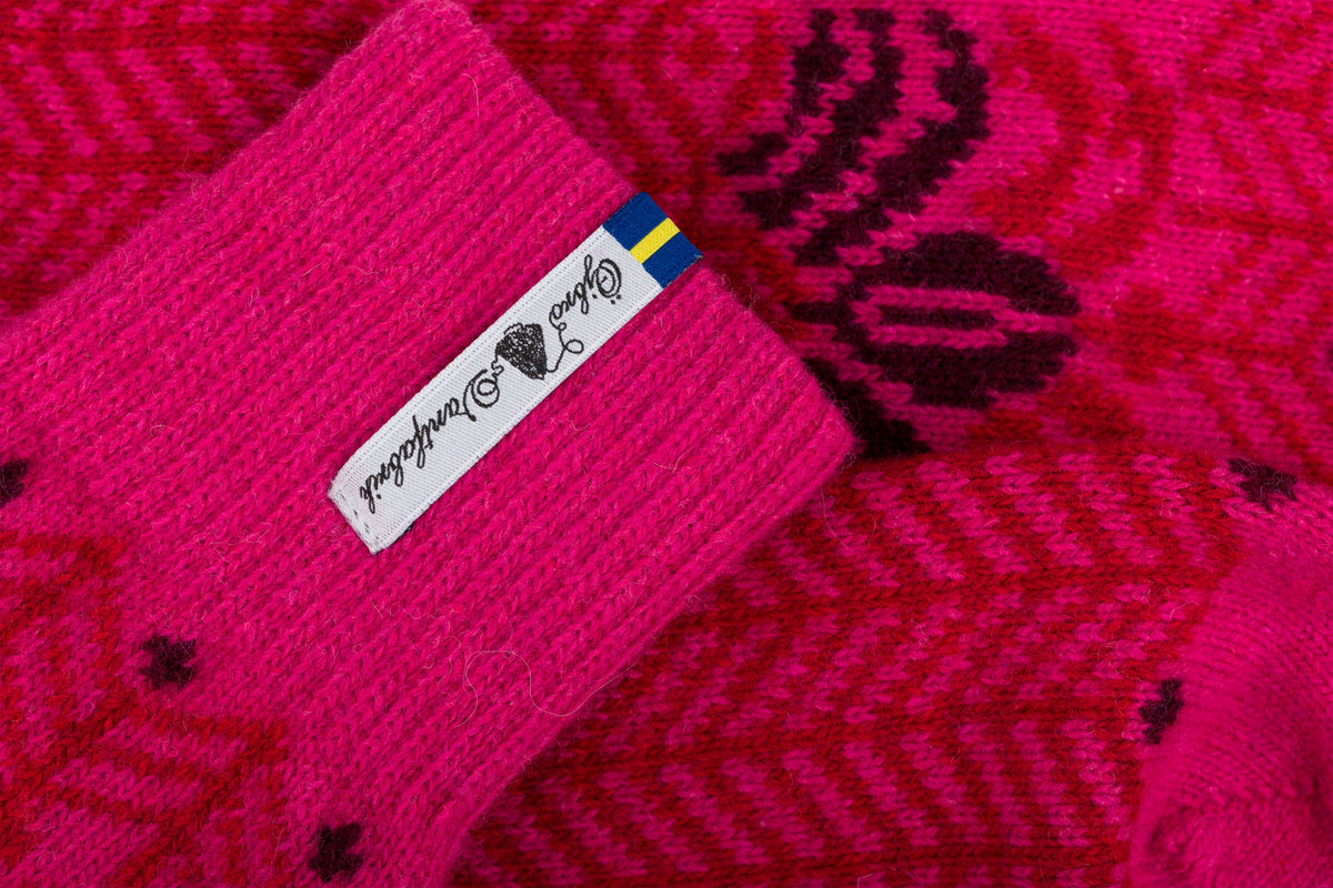 Close-up of a bright pink knit socks with a white fabric label and a small Swedish flag, showing the knit texture and patterned fabric.