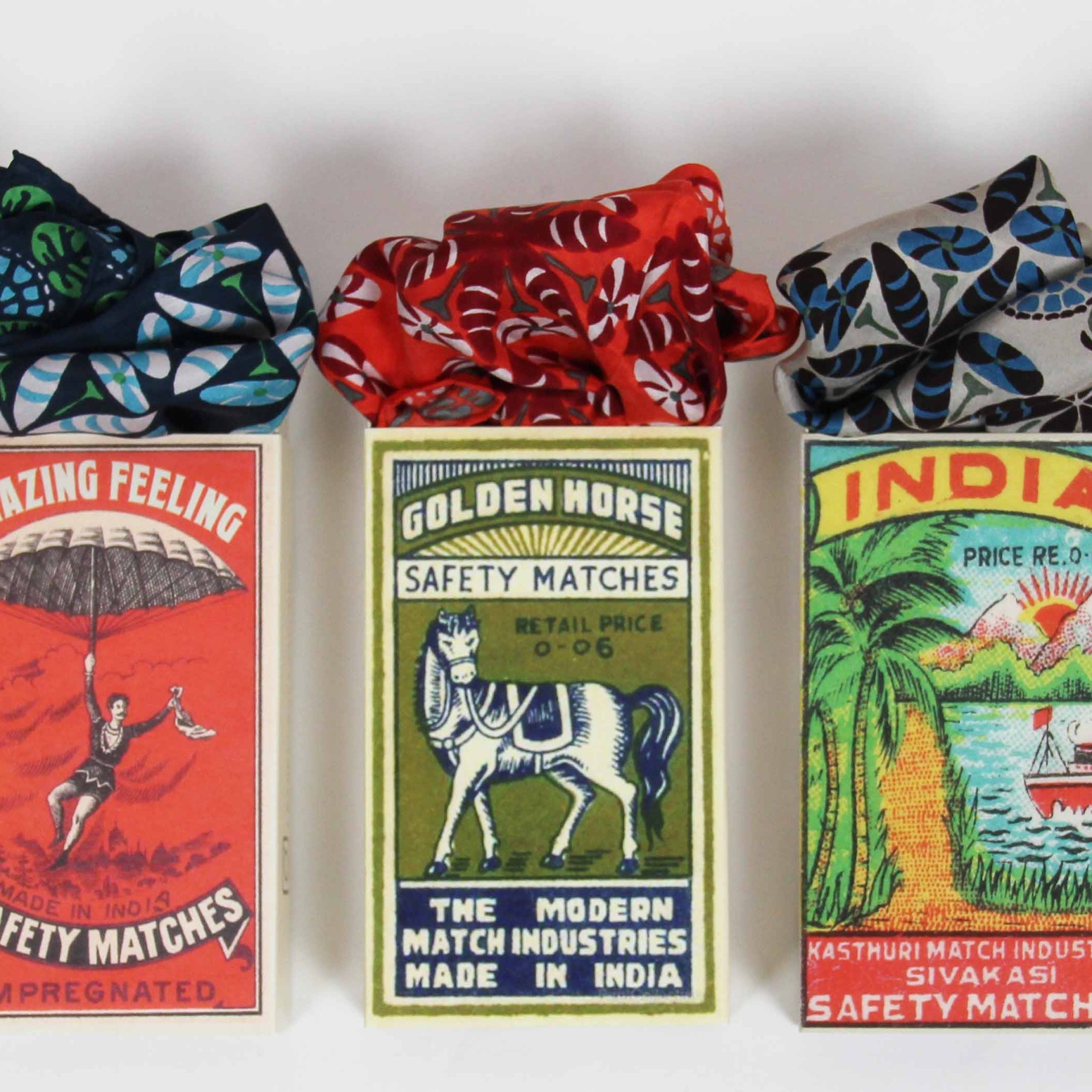 Three vintage matchboxes with colorful designs and text on a white background