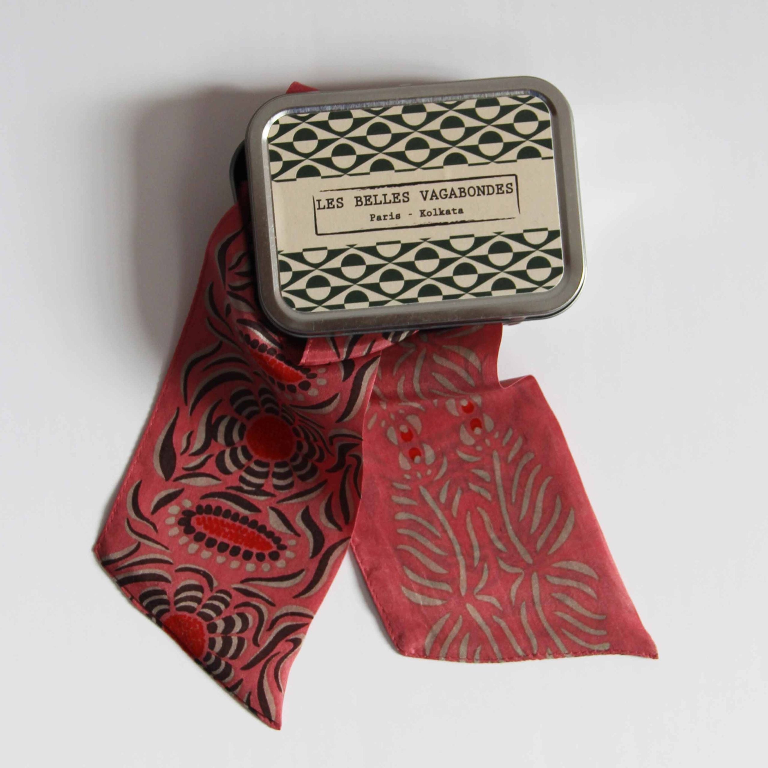 Small tin with decorative lid featuring 'Les Belles Vagabondes' branding, wrapped with a red patterned ribbon on a white background.