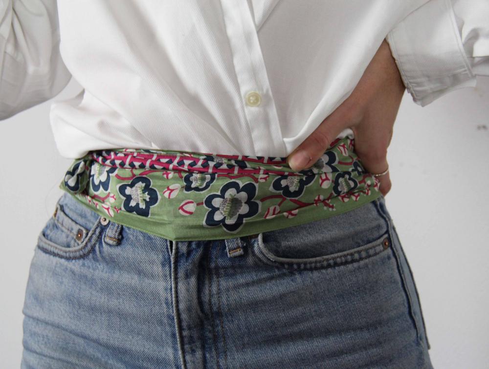 Person wearing a white shirt and blue jeans with a floral belt.