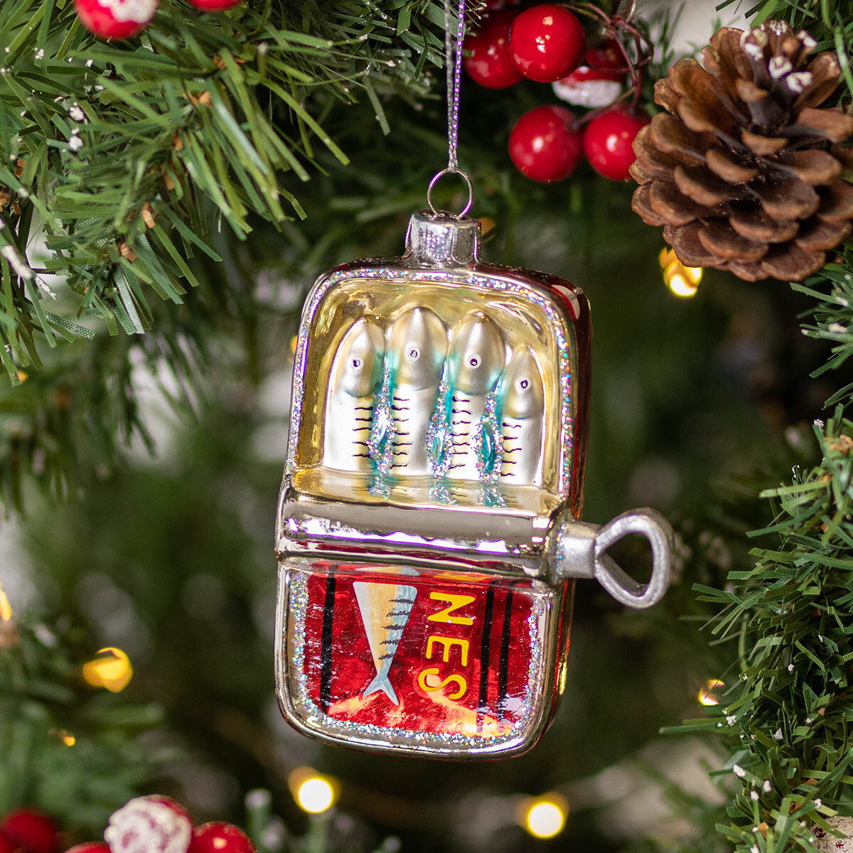 Decorative fishing lure ornament on a Christmas tree with lights and pine cones.