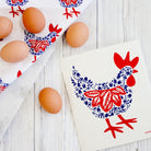 Eggs on a white surface with decorative towels featuring red and blue rooster designs.