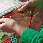 Close-up of hands tying a red ribbon on a green leaf-shaped object.