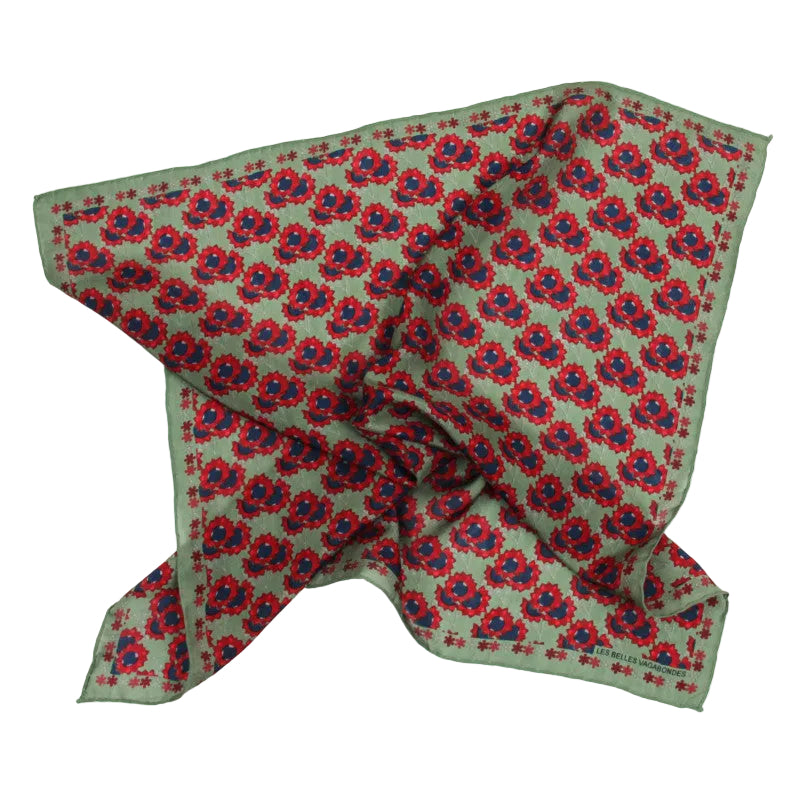 A square silk scarf with a green base, featuring a repeating red and blue floral pattern and a matching green border, laid out on a white background.