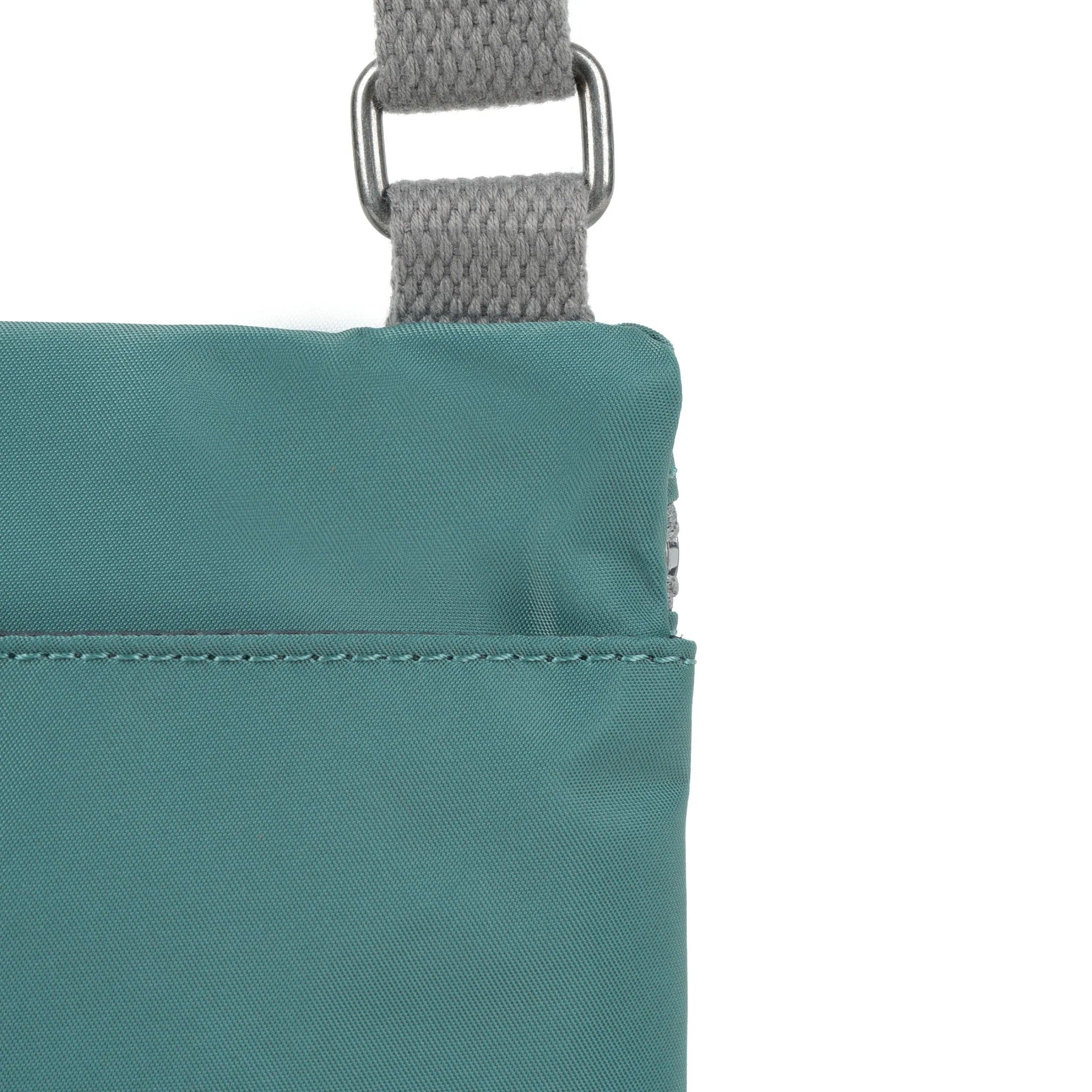 A close up photo of the back of a sage green bag, showing the grey strap and neatly stitched pocket opening.
