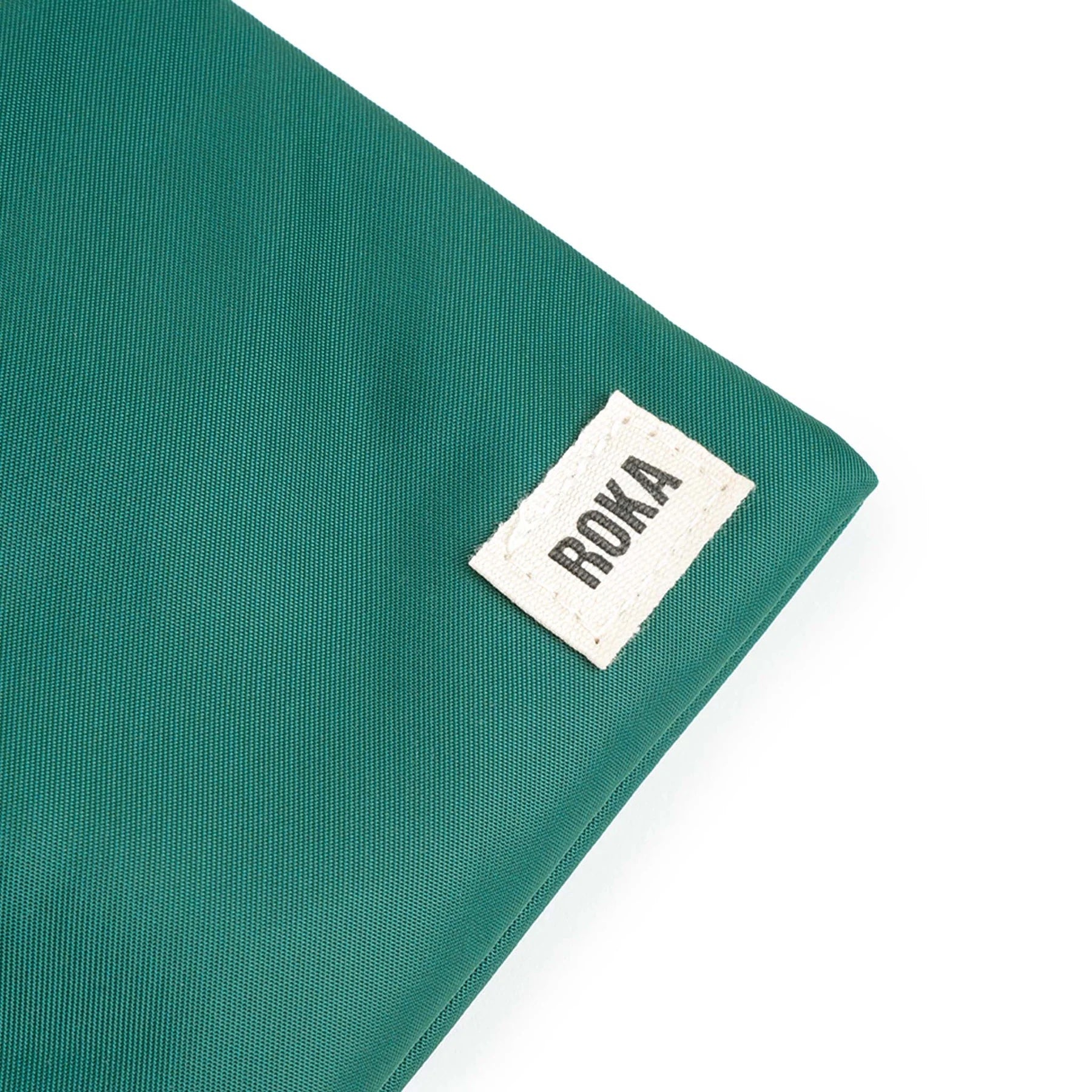 A close up photo of the bottom corner of a teal bag, showing the ROKA London label.