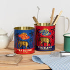 Two tin cans labeled 'Ceylon's Finest Tea Blend' on a wooden surface with kitchen items.