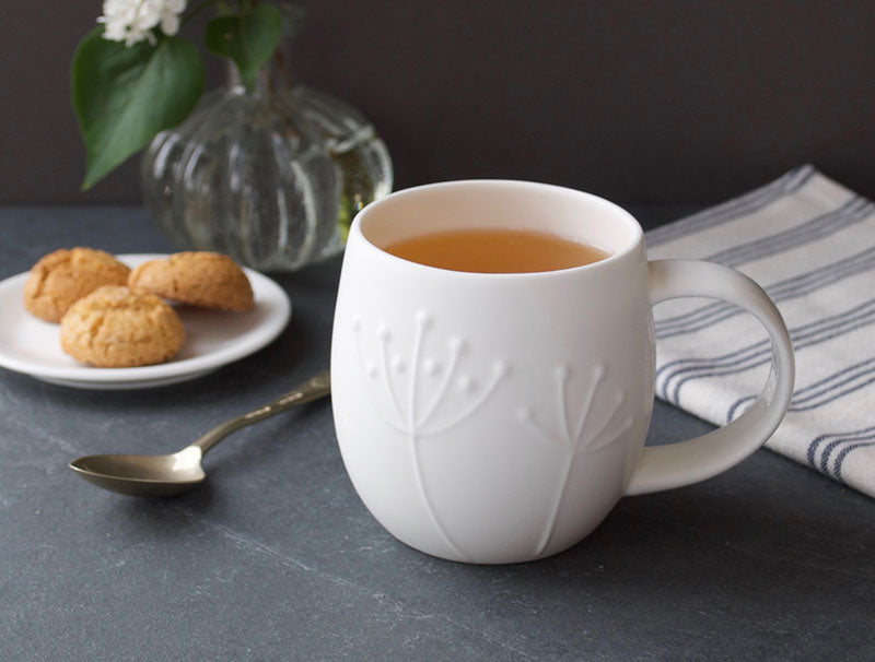 White mug with tea on a dark surface with cookies and a vase in the background