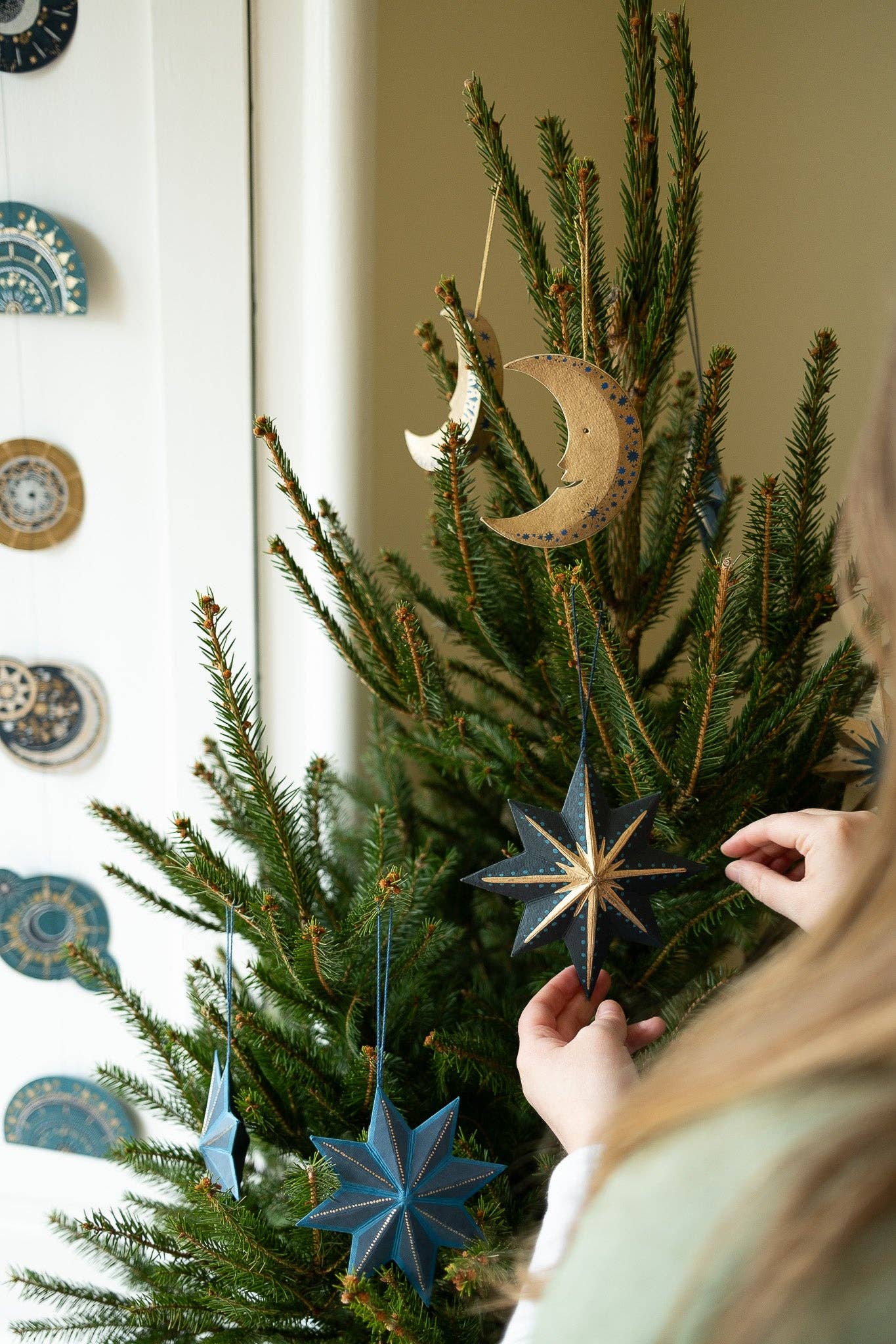 Person decorating a Christmas tree with star-shaped ornaments in a home setting.