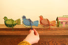 Hand interacting with colorful paper birds and a house on a wooden surface.