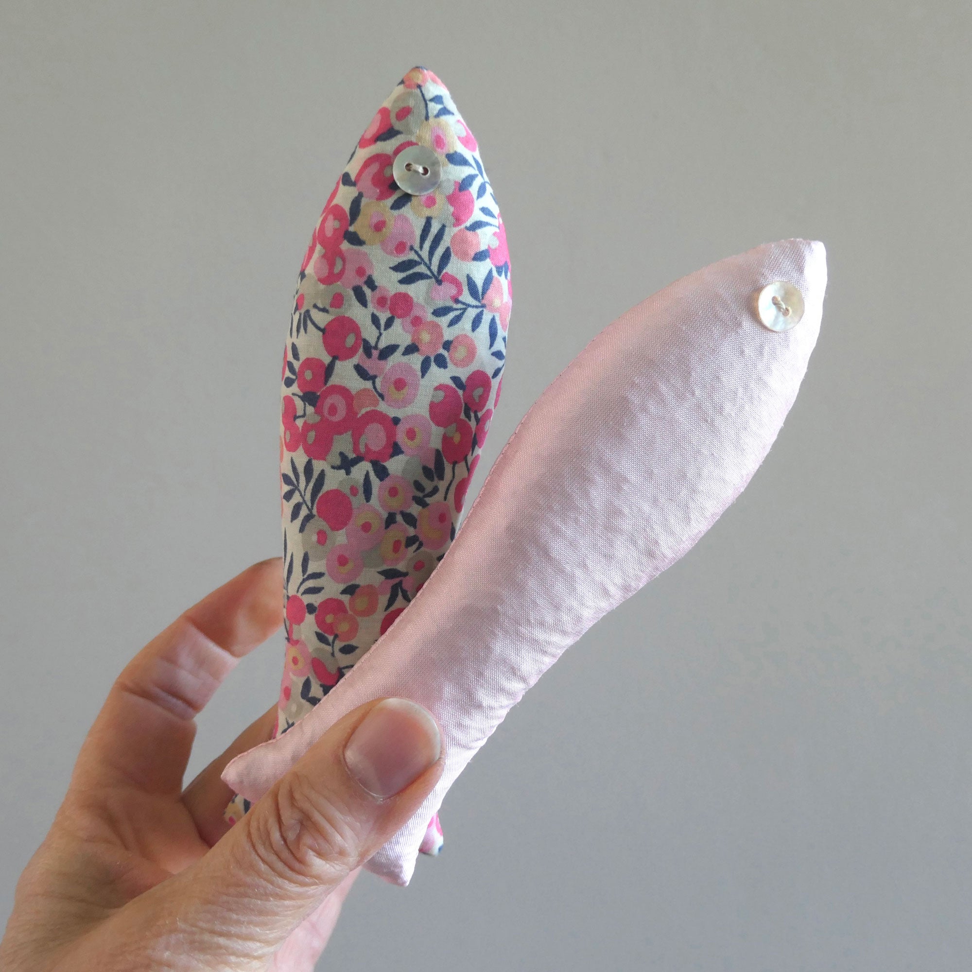 Hand holding a two floral-patterned sachets in pink against a plain background