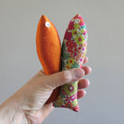 Hand holding two cotton and silk sachets in orange, green and red on a plain background