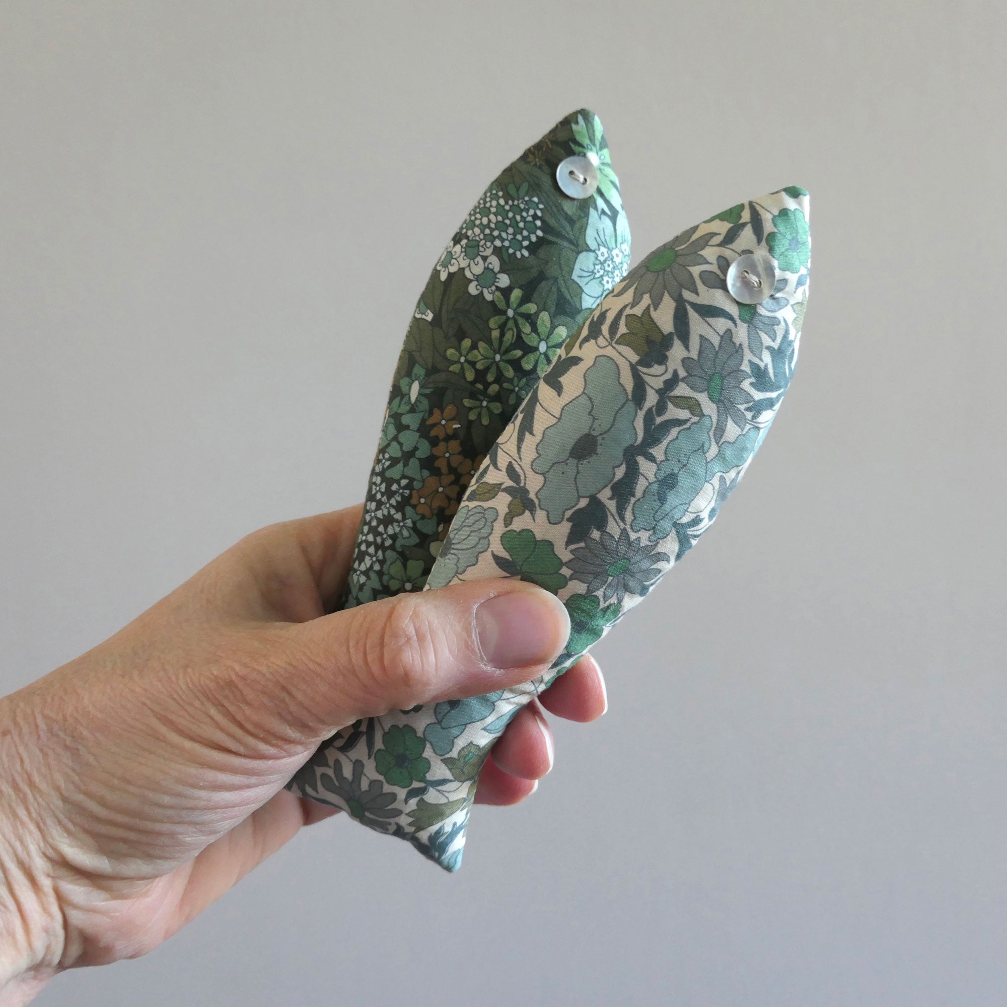 Hand holding two floral-patterned fish against a plain background