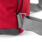 Close-up of a grey strap fastening on a red bag shown on a white background