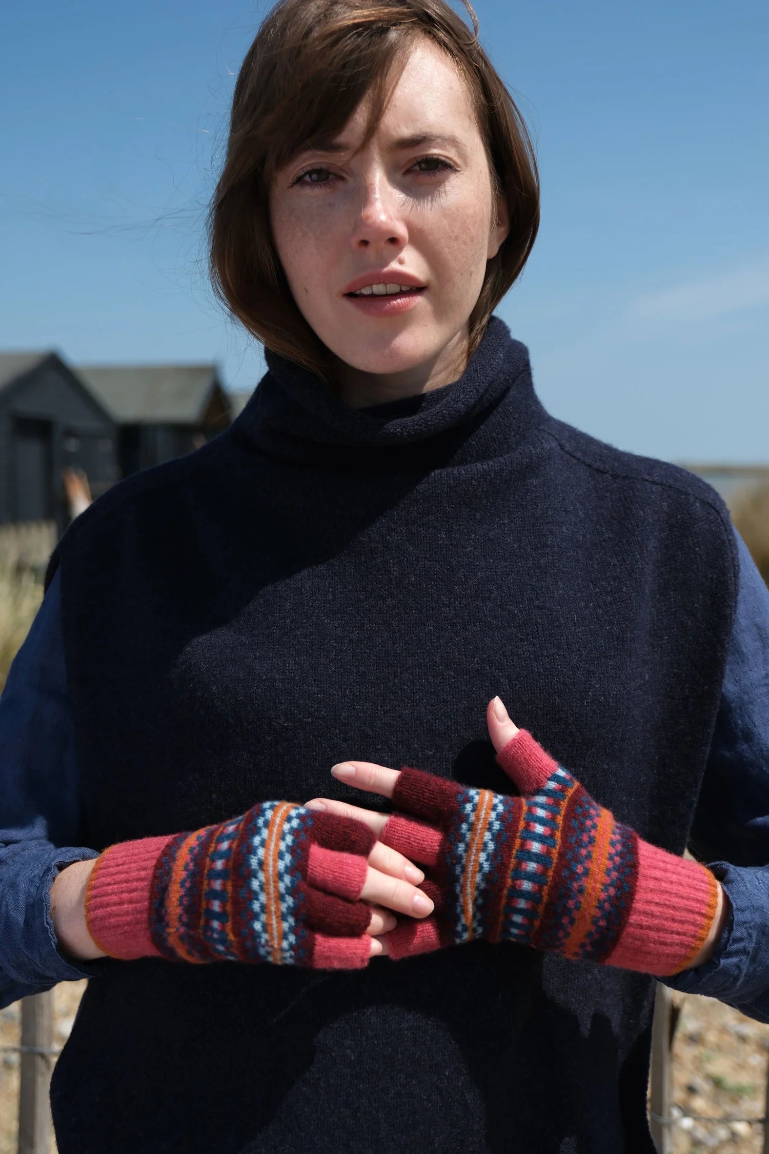 Woman wearing a dark blue sweater and colorful knitted gloves outdoors.