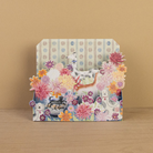 Decorative card with floral design and animal illustrations sat on a wooden surface.