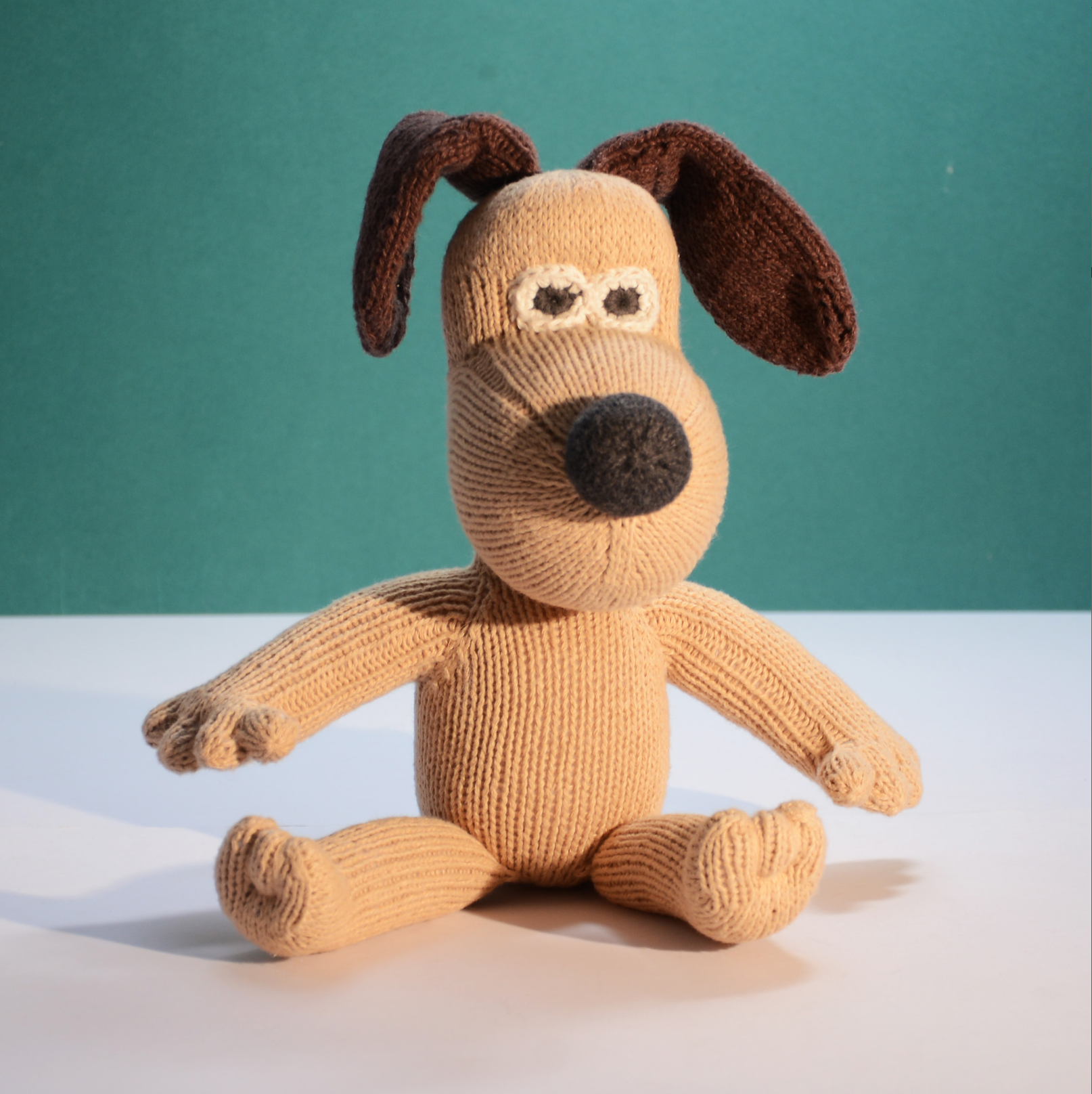 A knitted dog plush toy with floppy dark brown ears, a tan body, and a black nose.