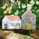 Two greeting card houses with colourful designs on a natural background with flowers.