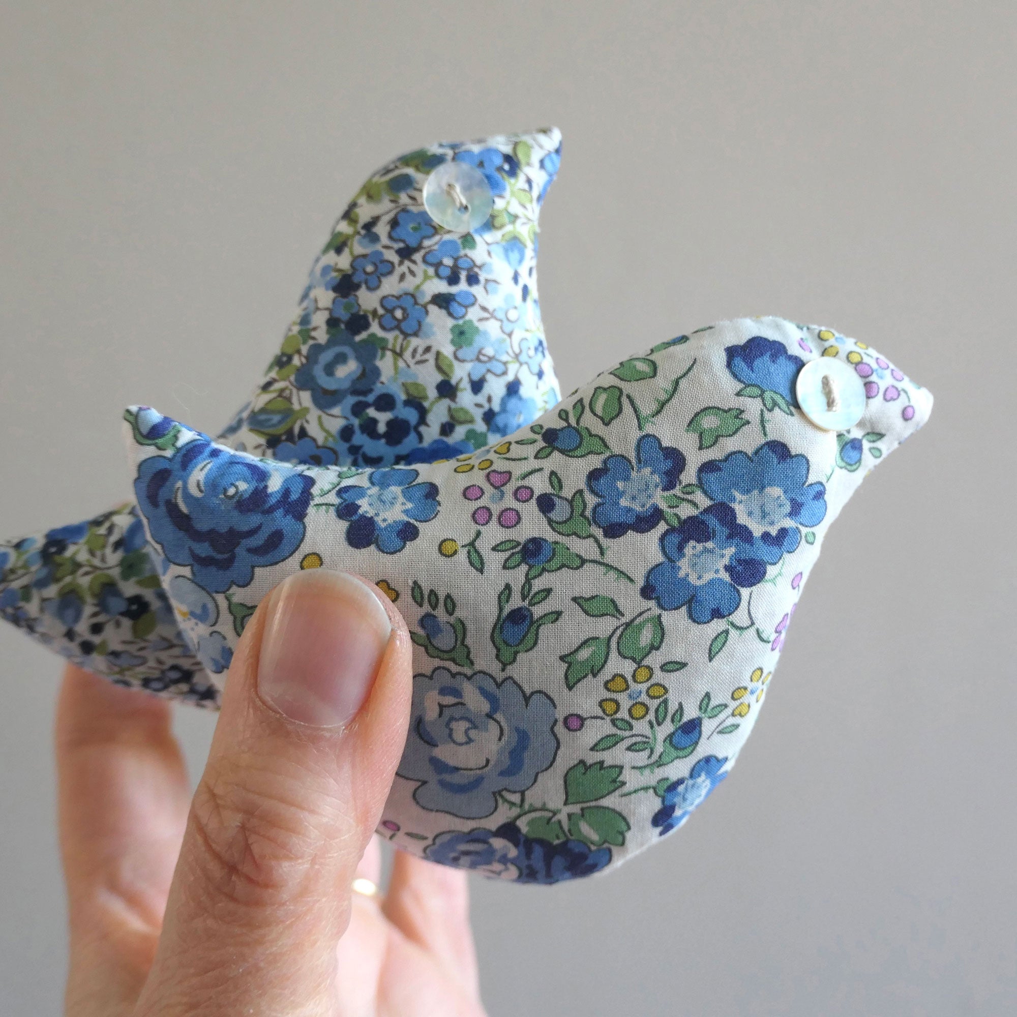 Floral-patterned fabric bird held by a hand against a plain background