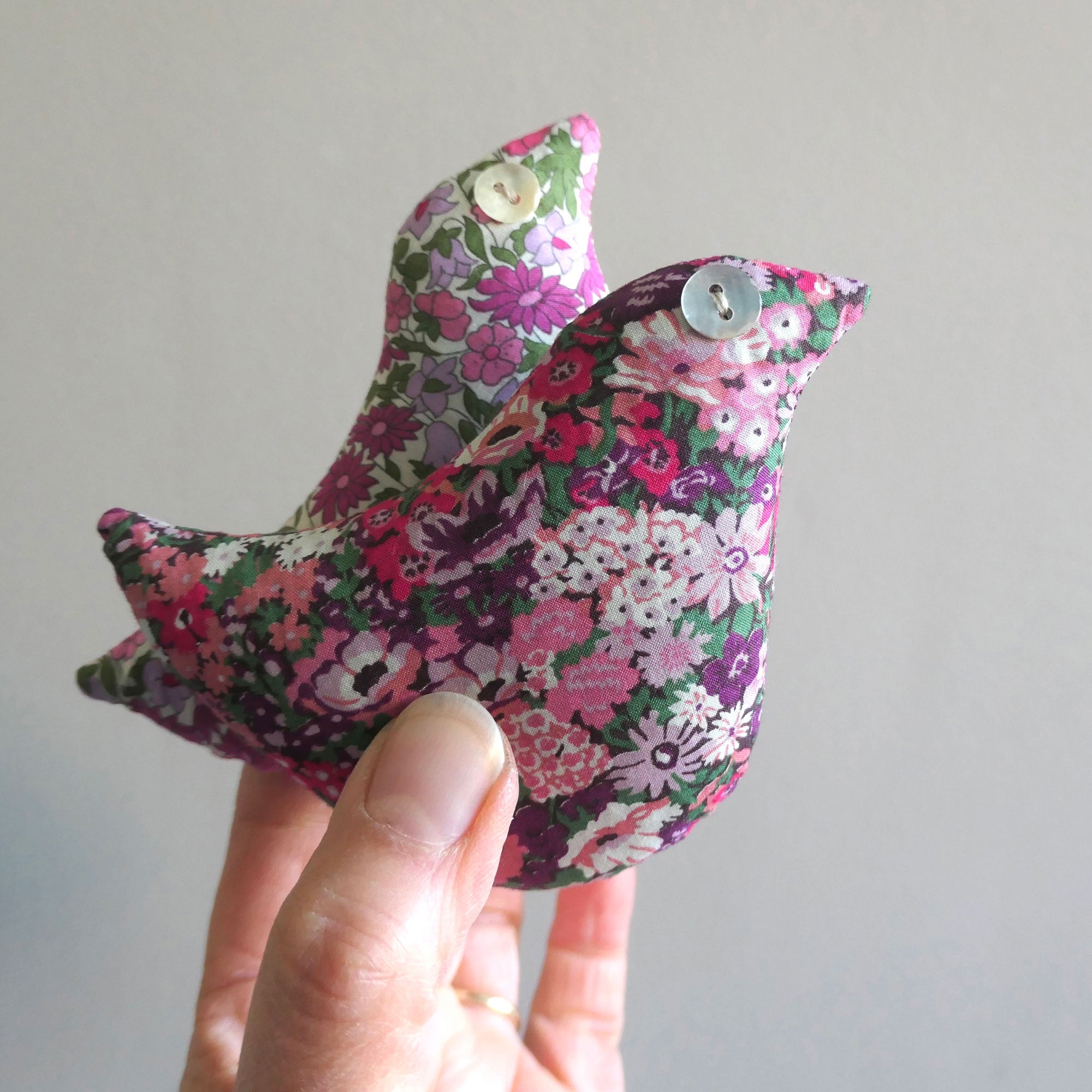 Pink floral-patterned bird-shaped lavender sachet held by a hand against a plain background