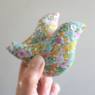 Handmade fabric bird with yellow, orange and green floral pattern held by a hand against a plain background