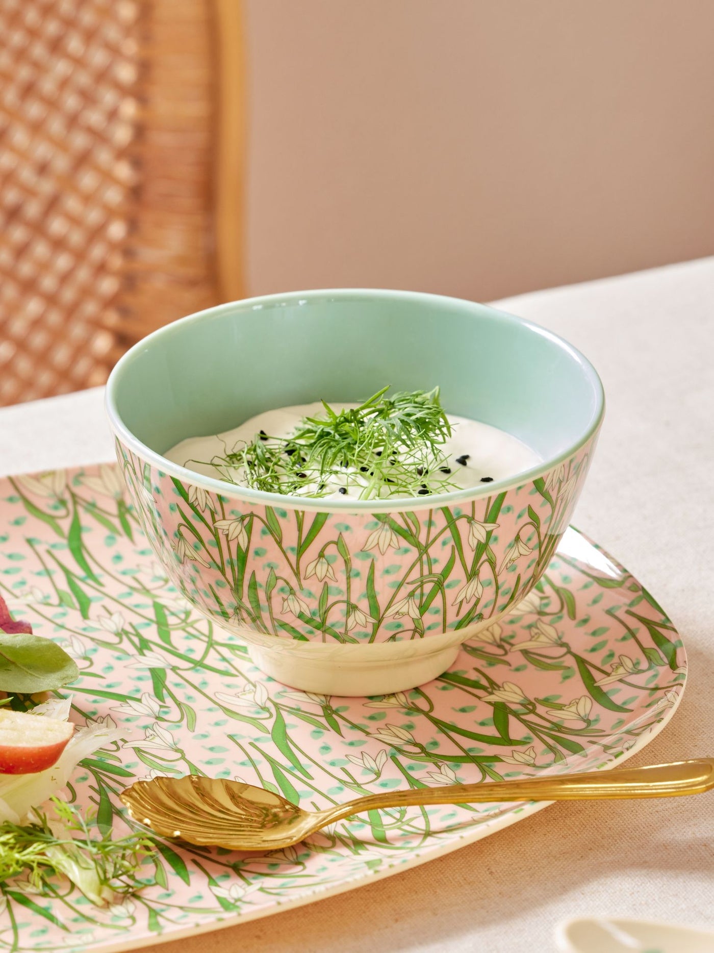 Bowl with green leafy garnish on a pink floral plate with a gold spoon