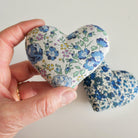 Hand holding a floral-patterned heart-shaped lavender bag against a plain background