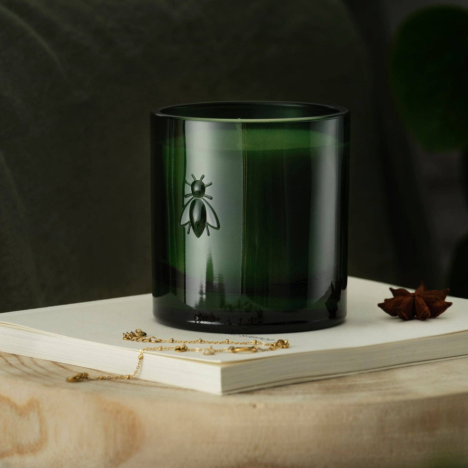 Dark green candle with a bee logo on a wooden surface and book