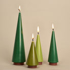 Set of four green tree-shaped candles with flames on a beige background