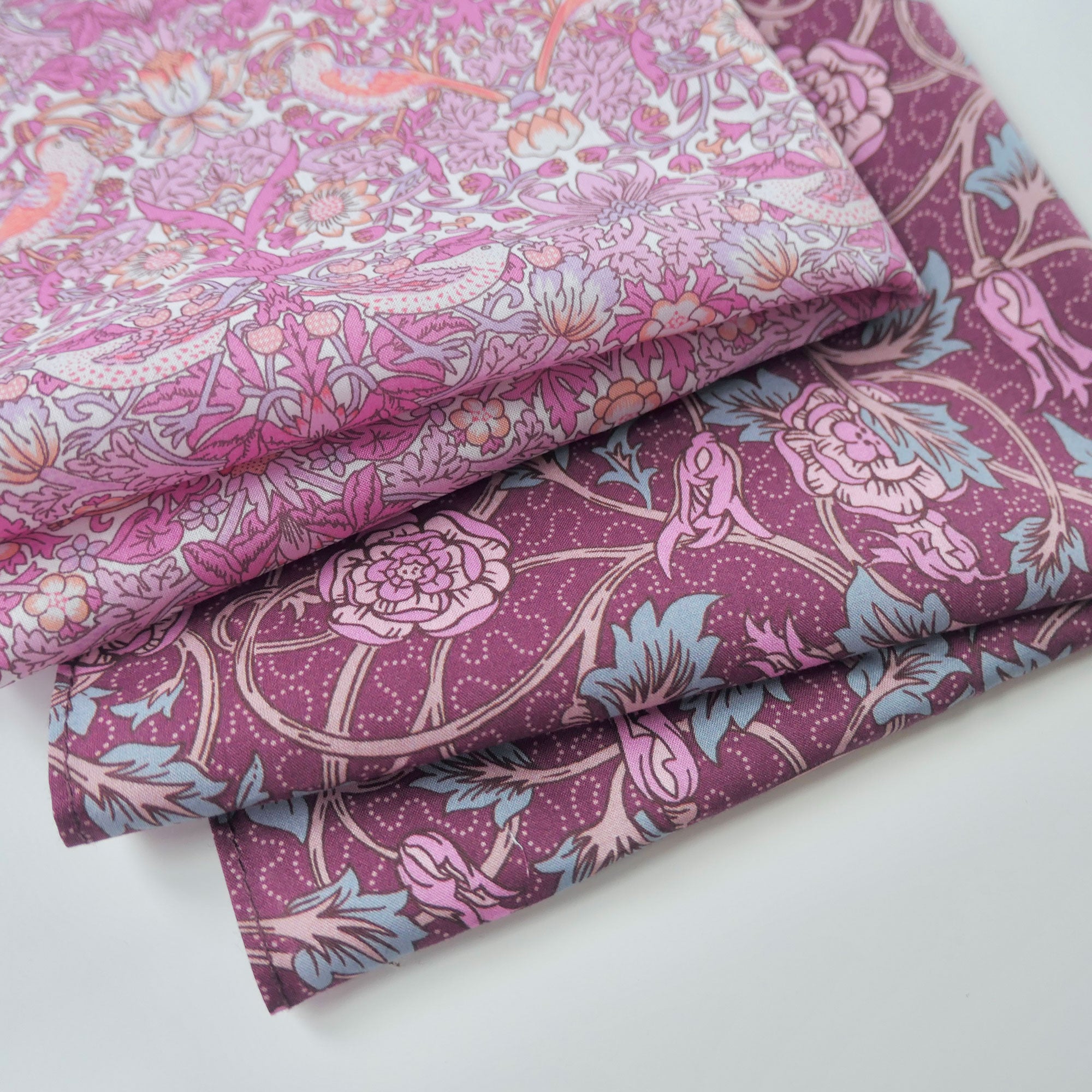 Two pieces of pink and purple floral fabric on a white background