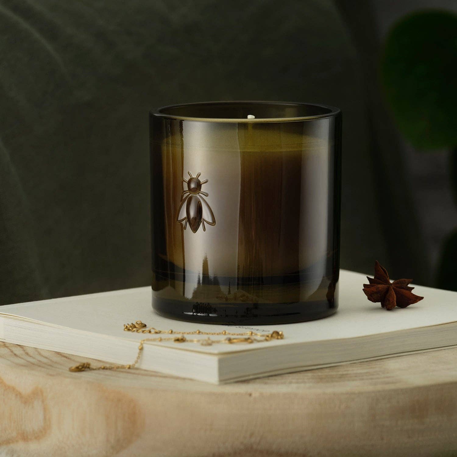 Candle with a bee design in a green glass container on a plain book