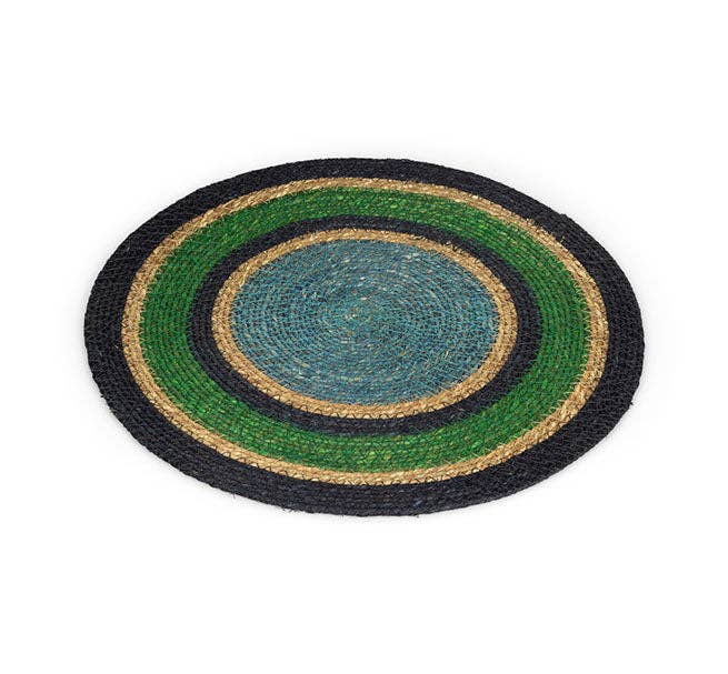 A round braided mat with concentric rings of black, green, natural tan, and a blue-grey centre, shown on a plain white background.