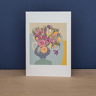 Notecard featuring artwork by Jane walker ‘Purple and Pink’ featuring poml, purple and gold-toned flowers in a blue dotty vase. 