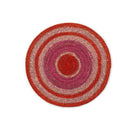 A round woven placemat with concentric circular stripes in red, pink, and beige, photographed from directly above on a white background.