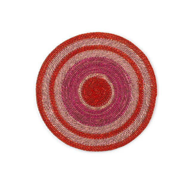 A round woven placemat with concentric circular stripes in red, pink, and beige, photographed from directly above on a white background.