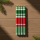 Set of four striped candles in green, red, and white on a wooden surface with pine branches.