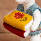 White plush toy holding a yellow book with a red flower design on a blurred background