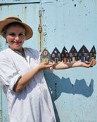 Woman in a white dress and hat standing in front of a blue wall with a small village mural.