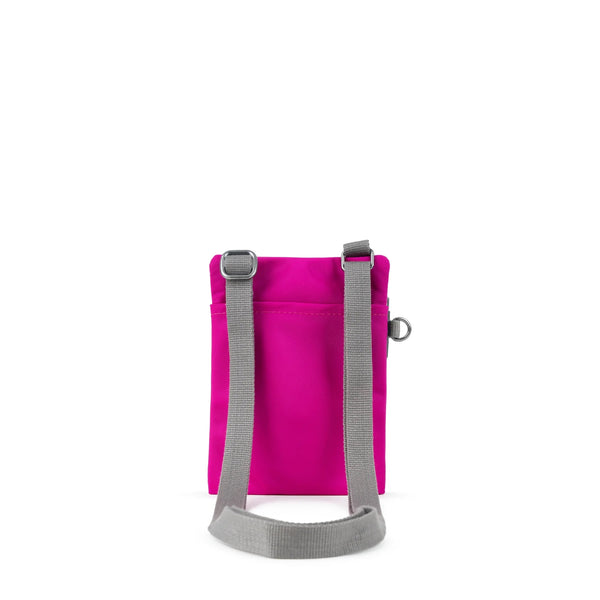 A photo of the back of a small rectangular bright pink pocket bag. It has a pocket and grey straps.