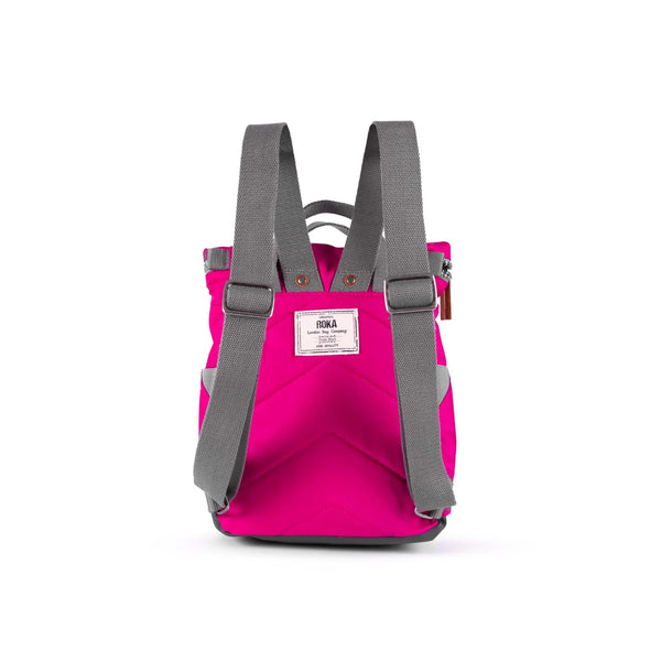 Photo showing the back of a small bright pink coloured backpack. The straps and handles are grey and there’s a small fabric label with the ROKA logo on.