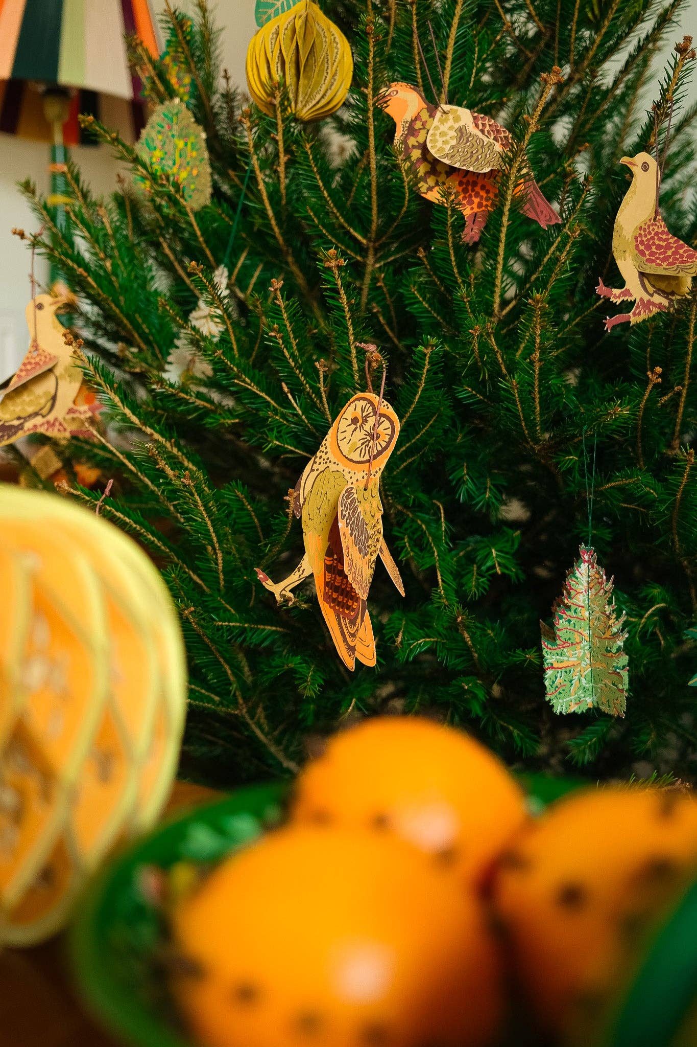 Decorative Christmas tree with colorful ornaments and tangerines on a table.